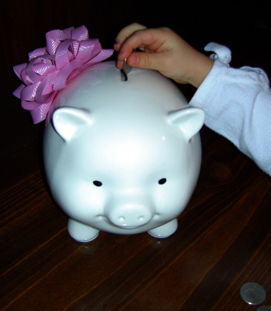 picture of small child placing money into a white piggy bank
