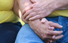 a couple holding hands together nicely while sitting on a bench. Both are wearing yellow shirts and he is wearing jeans. Gives a feeling of being together and secure in their retirement.