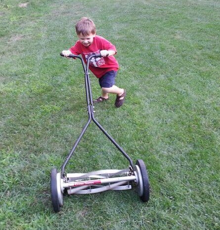 small boy pushing a manual lawn mower on the grass